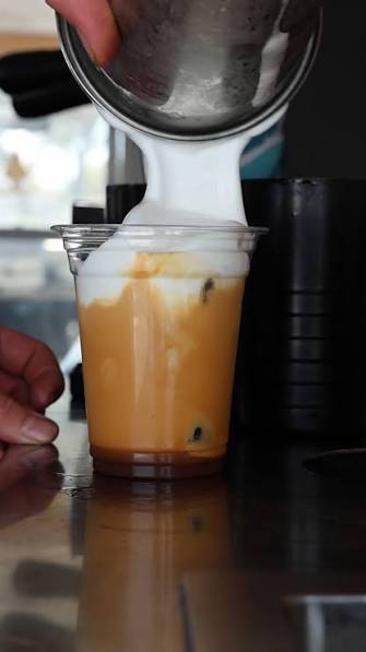 Barista pouring silky foam into a freshly prepared Brew on Wheels coffee drink